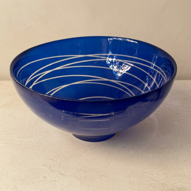 Cuenco azul con líneas decorativas, vista inclinada con base clara y pared beige
